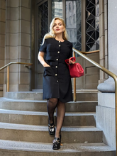 a lady wears a black mini dress with a red handbag and black loafers